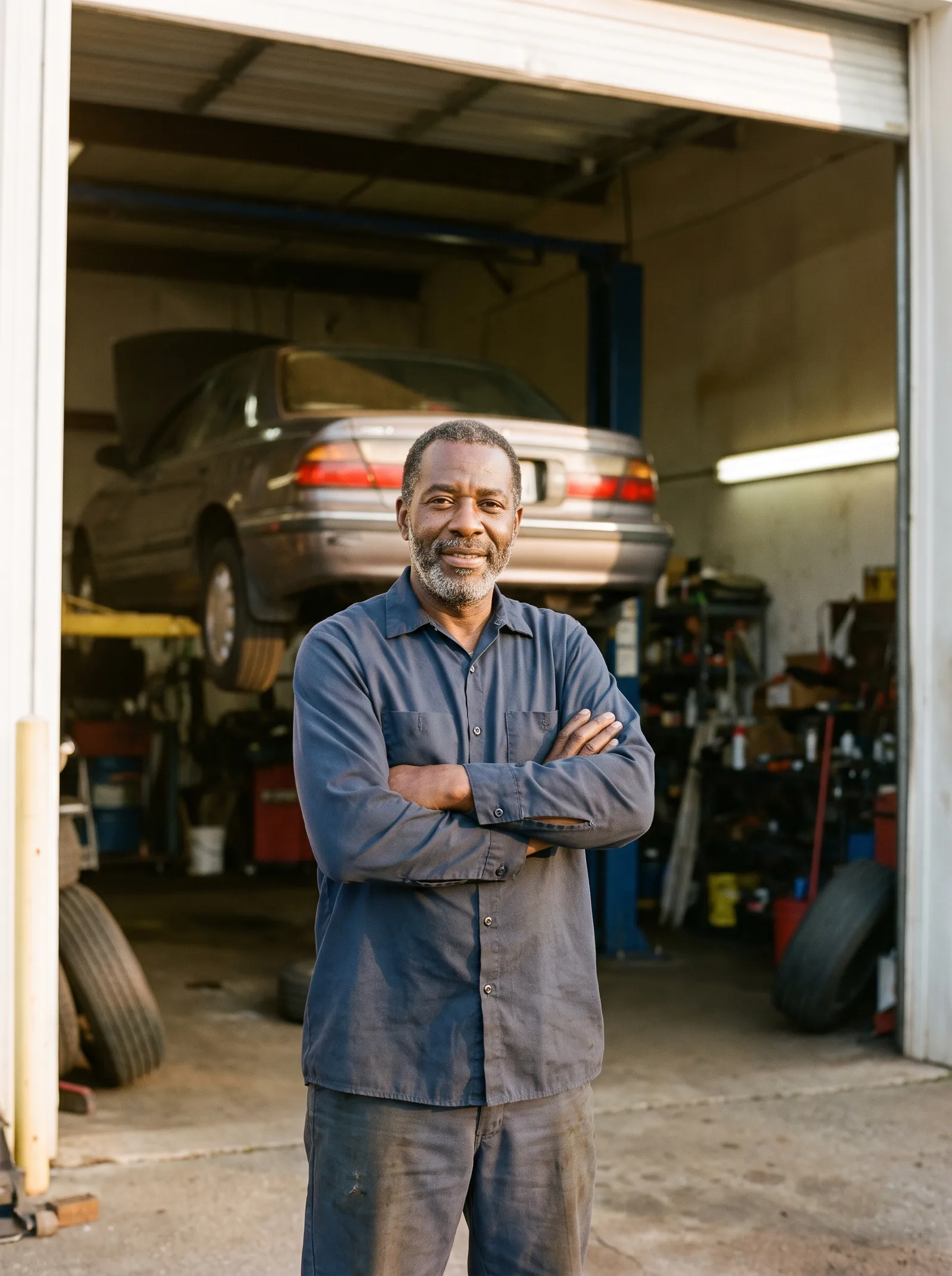 An auto shop owner with crossed arms in his garage doorway